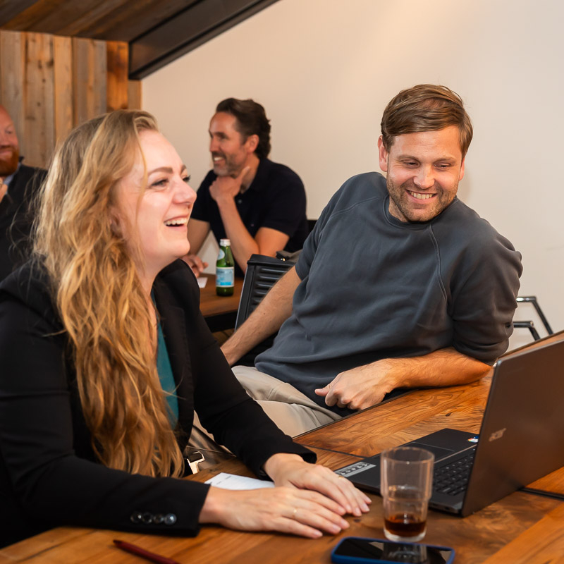 Mensen kijken vrolijk vooruit terwijl ze op een laptop werken
