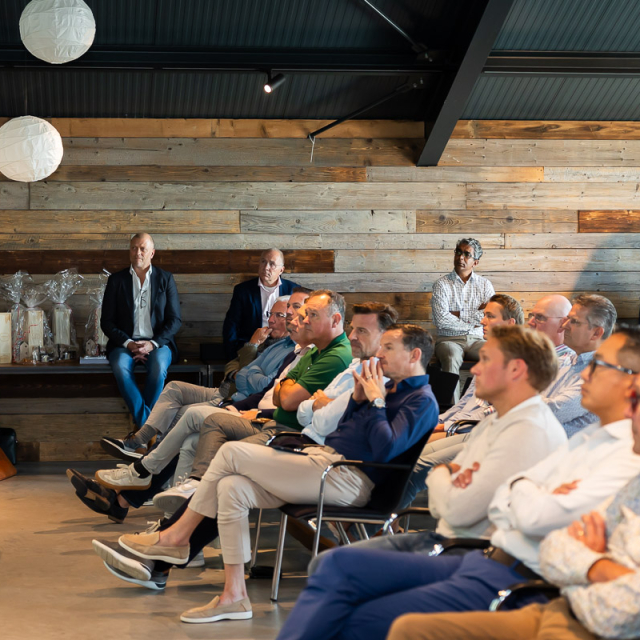 Mennsen zitten en luisteren naar een man die staat en praat door een microfoon