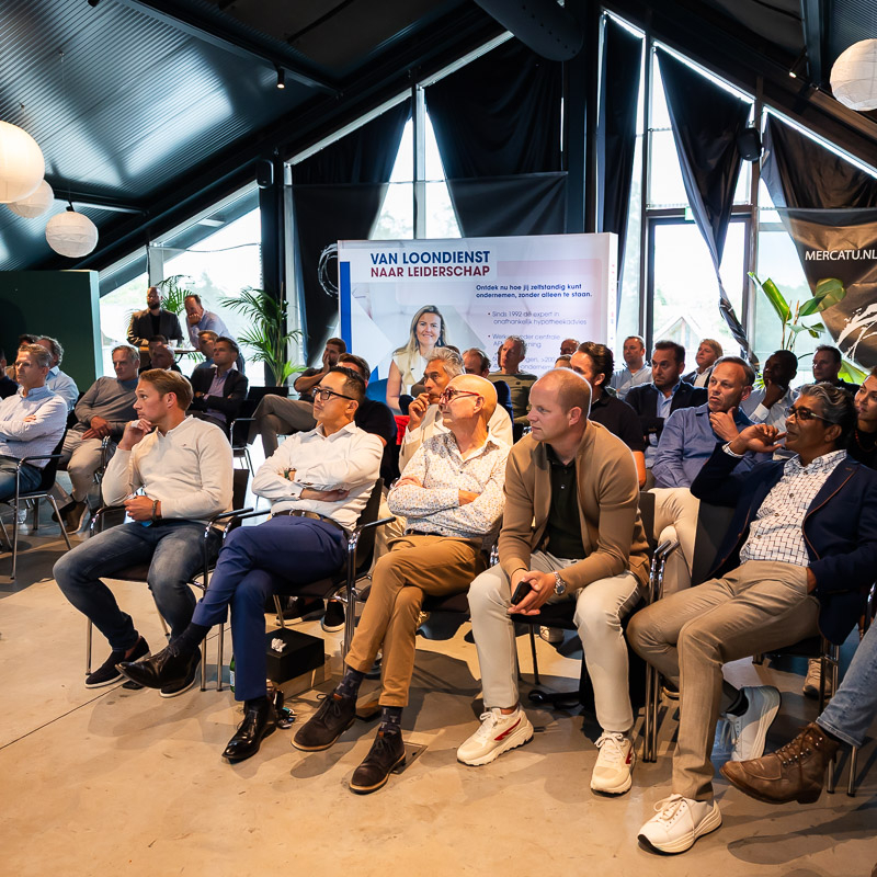 Mensen zitten in een zaal en kijken schuin naar voren