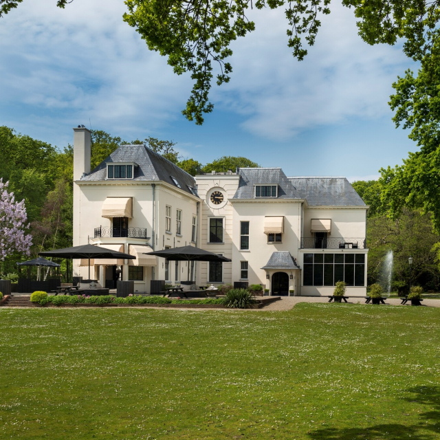 Wit landhuis omringt door groen gras en bomen