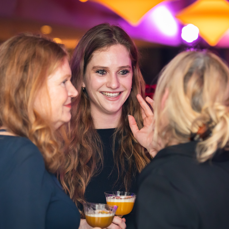 Drie vrouwen staan met elkaar in gesprek en lachen